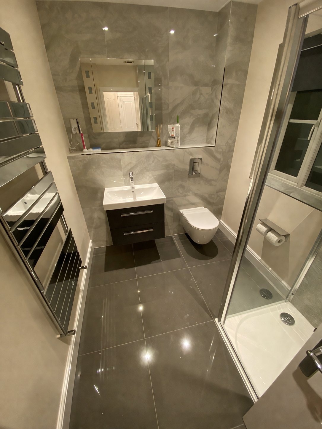 Shower room with grey large format tiles, wall hung vanity and chrome towel rail
