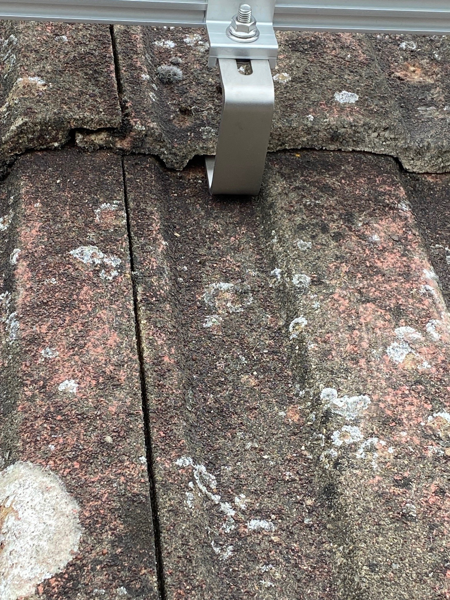 Close up of solar panel roof bracket and mounting hardware on aged tiles